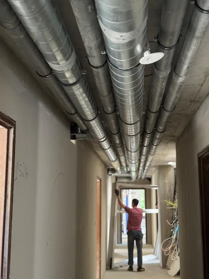 Artisan gintáqua dans un couloir équipé de réseaux d'évacuation et de ventilation fixés au plafond