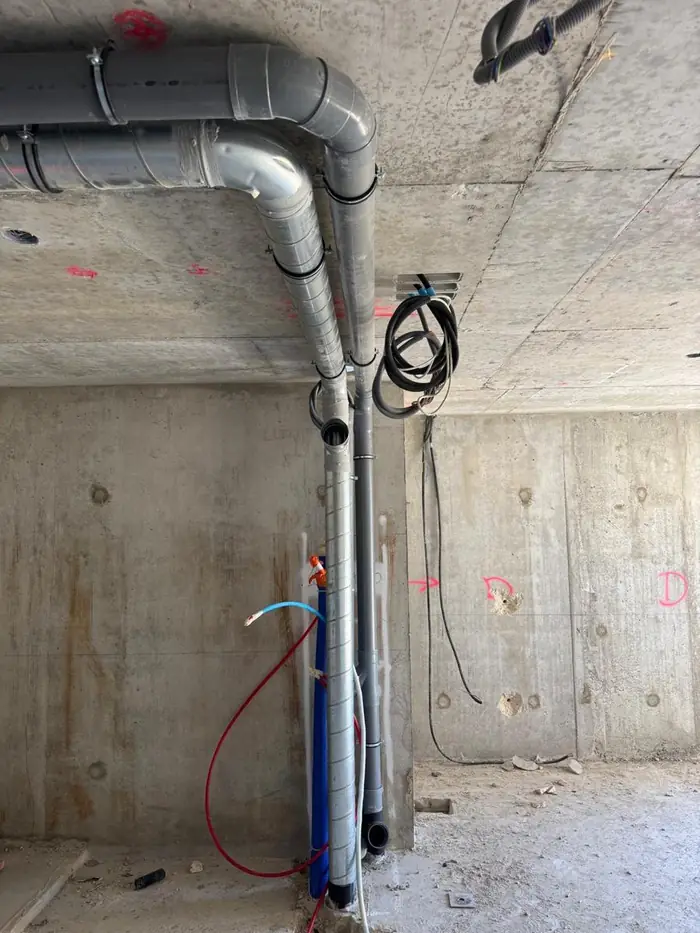 Descente d'évacuation PVC et alimentations en eau PER rouge et bleue posées le long d'un mur
