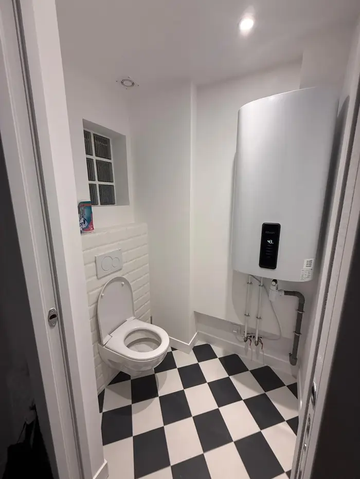 WC suspendu avec bâti-support et chauffe-eau mural neuf, sol carrelé en damier noir et blanc