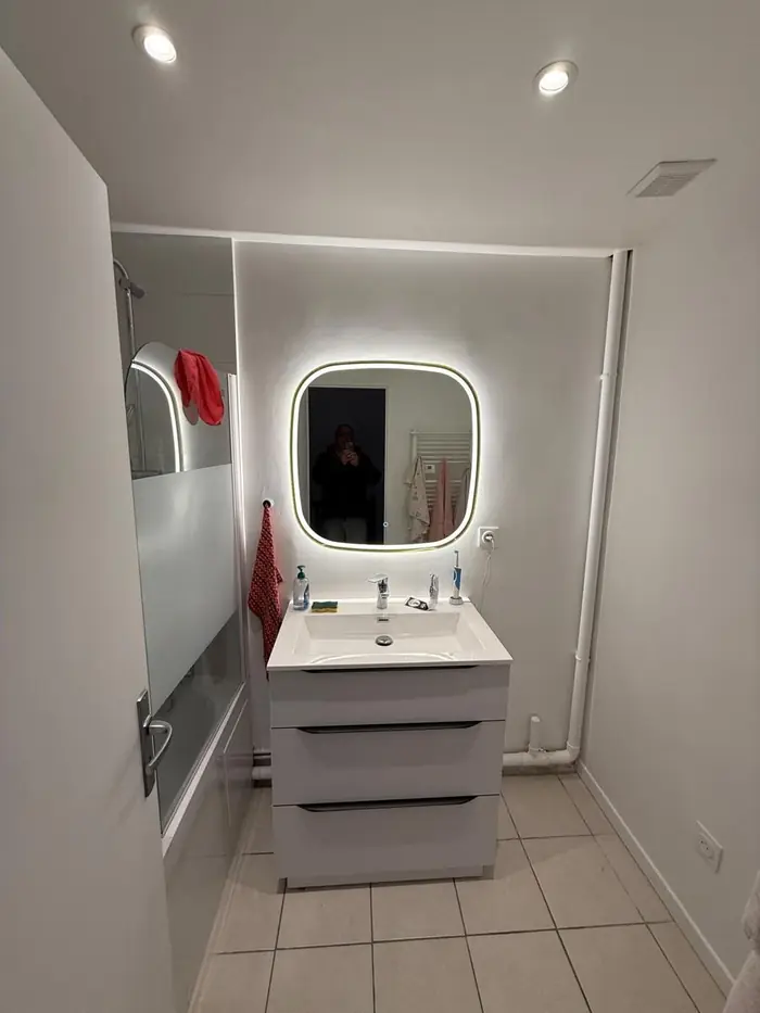 Salle de bain rénovée : meuble vasque blanc à tiroirs, miroir LED rétroéclairé, pare-baignoire et spots encastrés