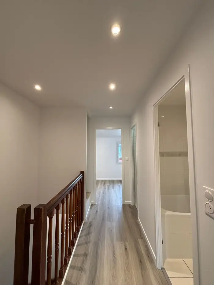 Palier d'étage rénové avec sol aspect chêne clair, rampe en bois et vue sur une chambre et la salle de bain